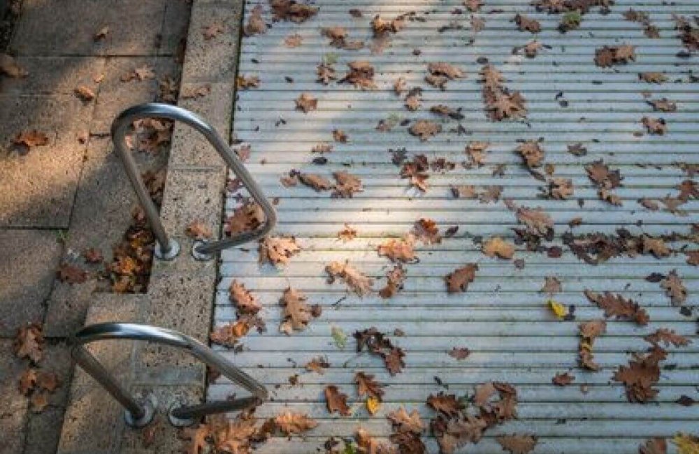 Volet roulant recouvrant une piscine, avec des feuilles mortes dessus.